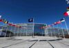 Poland Nears Permanent U.S. Military Base NATO headquarters with member flags in front under a clear blue sky