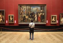 A person standing in an art gallery, observing a large historical painting surrounded by other artworks