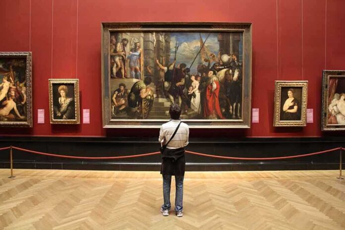 shutterstock_235506019-1 A person standing in an art gallery, observing a large historical painting surrounded by other artworks