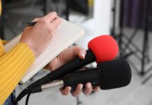 Three Iranian Tankers Hit as Gulf Tensions Rise Journalist holding two microphones while writing in a notebook