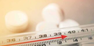 Glass thermometer with red indicator near 39°C beside white tablets