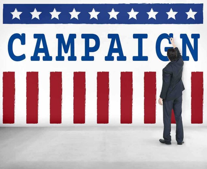 Man in suit writing on large campaign banner with stars and stripes