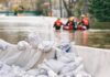 Sandbags stacked near a flooded street with rescue workers in a boat