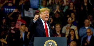 Donald Trump speaking at a rally behind a presidential podium