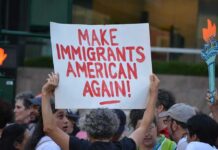 Viral Anti-ICE Clip Highlights Protest Tensions Teddy Williams at a protest holding a sign reading 'Make Immigrants American Again'