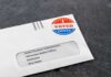 Utah Official Raises Alarm Over Voter Data Absentee ballot envelope with I Voted sticker on dark surface