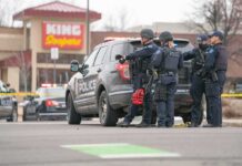 Police officers gather beside a patrol SUV at a taped-off scene