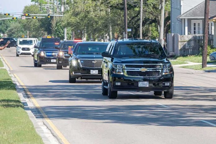 motorcade of black SUVs driving down a suburban street
