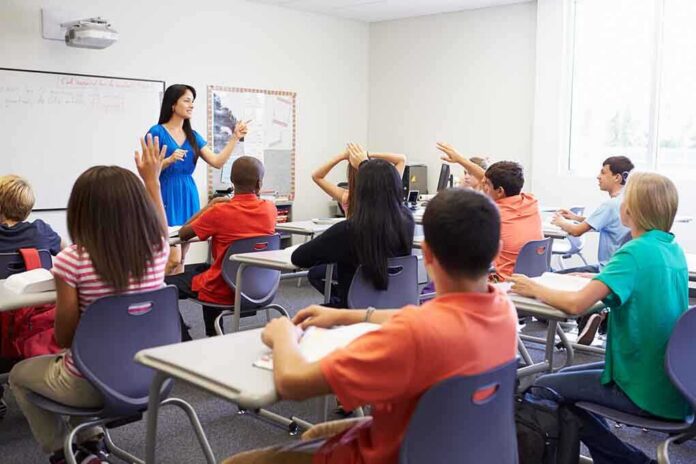 shutterstock_199144970-1 Teacher leading classroom discussion with students raising hands