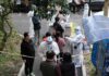 Christian Jones and others wait at an outdoor COVID-19 testing site with staff in protective suits