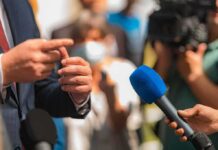Violent Remarks Spark Political Backlash Person in suit speaking to reporters with microphones
