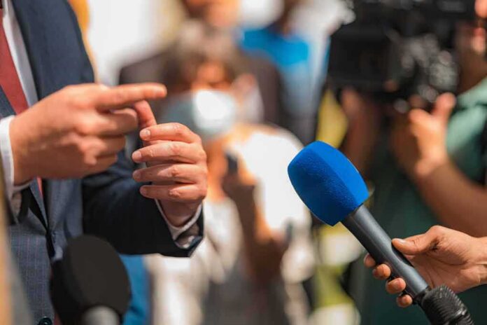 Person in suit speaking to reporters with microphones